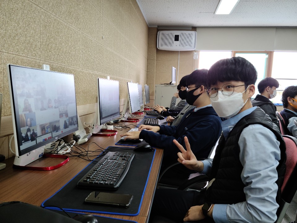 P-TECH student wearing face mask and showing a peace sign with his hand in front of a computer